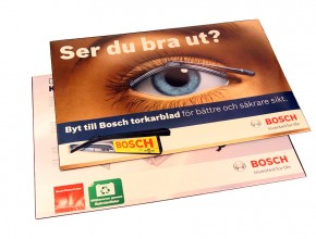 Skrivbordsunderlägg med insvetsad trycksak och pappförstärkning mellan glasklar plast och färgad plastundersida. Format: 590x400mm.