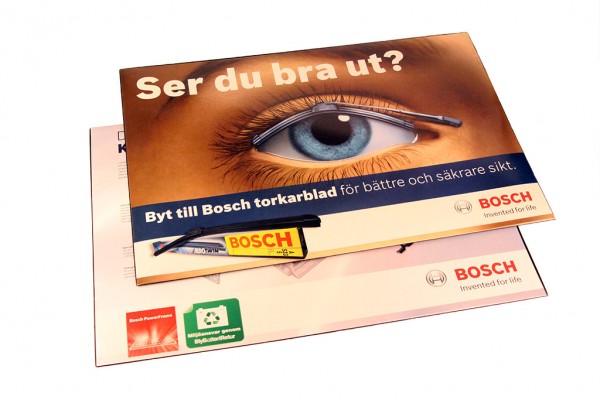 Skrivbordsunderlägg med insvetsad trycksak och pappförstärkning mellan glasklar plast och färgad plastundersida. Format: 590x400mm.